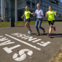 Hardlopers opgelet! Een parcours afleggen kan gewoon in de wijk. Er is een route van bijna 2 kilometer uitgestippeld.  Sinds kort staan in het Gerrit Rietveldpark grote cijfers op de weg: een circuit van 1.900 meter met een duidelijke start en finish, en ertussen om de 100 meter cijfers met de afstand. ’Een makkelijke manier om te trainen’, vertelt Saskia Warmer van Loopgroep Nesselande. Samen met een sporter van atletiek- en triatlonvereniging Trackstars Nesselande diende ze een bewonersinitiatief in voor de route, die onder andere via het Korfoepad loopt. ‘Het is een mooie stimulans voor alle Nesselanders om te gaan rennen. Ze kunnen het parcours zelf gebruiken. En voor de trainingen van onze hardloopgroep en Trackstars is het superfijn. We hebben al een kleiner parcours en met deze nieuwe route is ons trainingsgebied verbeterd.’   Blijven fit Van beginnend hardloper tot marathonloper: iedereen kan trainen bij de loopgroep bij de Zevenhuizerplas. ‘Mensen kennen ons wel; we rennen wekelijks met zóveel lopers met gele hesjes aan door de buurt’, vertelt Saskia. ‘We hebben trainers in dienst en gebruiken een handig muntensysteem. Doe je mee, dan kost het 1 muntje van 3,50 euro. Je hoeft dus geen lid te zijn. Ideaal toch? Mijn man en ik regelen alles rondom de loopgroep. We zijn gepensioneerd en hoeven er niet veel aan te verdienen. En we blijven er zelf fit bij natuurlijk.’  Sportboulevard Het parcours is helemaal op z’n plaats in Nesselande, vindt Saskia. ‘Nesselande is een enorme sportwijk. De Kosboulevard kun je met het sportpark en de skatebaan een sportboulevard noemen. En kijk maar eens naar de Zevenhuizerplas: we joggen er continu omheen met z’n allen.’